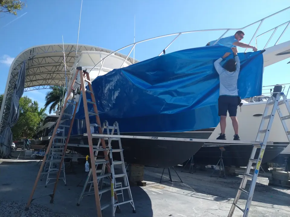 Two installers laying a blue vinyl wrap over a cruiser hull under a shed