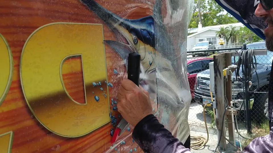 Installer peeling the transfer tape off gold lettering on a printed hull