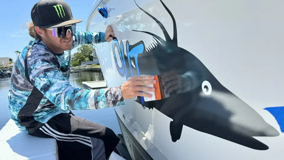 Installer applying a shrimp graphic beside a boat name on a white hull