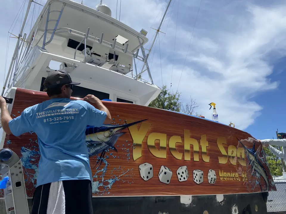 Installer squeegeeing the Yacht Sea faux-teak transom wrap onto a sportfish