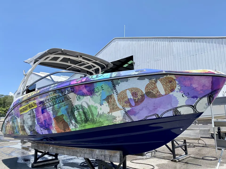 Wake boat in a full printed hundred-dollar-bill wrap on stands