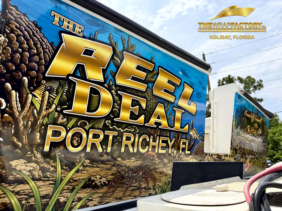 The Reel Deal, Port Richey FL lettering in gold over a reef-print boat wrap