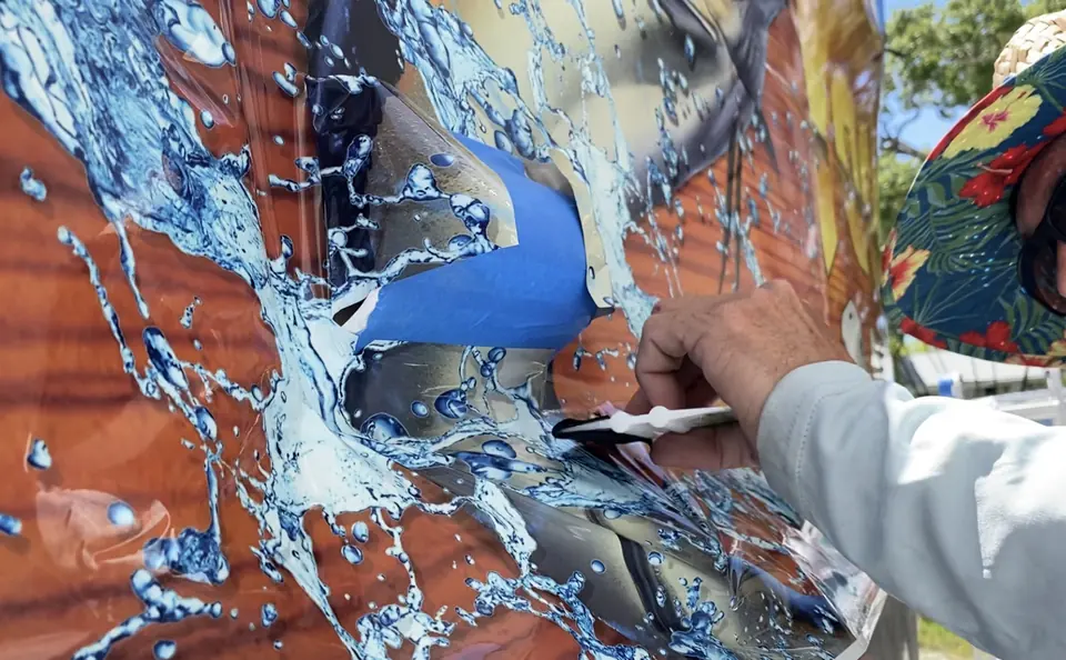 Hand with a squeegee laying a printed marlin graphic onto a hull