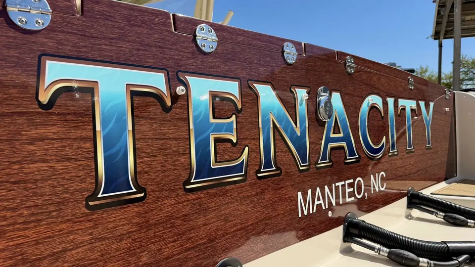 Tenacity, Manteo NC lettering in blue and gold leaf on a faux-teak transom